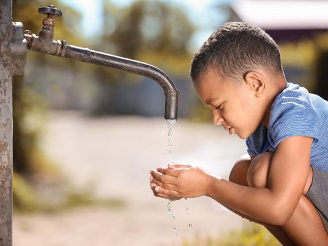 African American child drinking water from tap outdoors. Water s